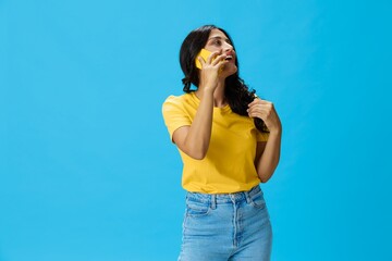 Woman with a phone in her hands with a yellow case on a blue background in a yellow T-shirt,...