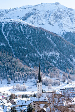 Small town with church under snow covered mountains with tres during winter in Zuoz, Switzerland.
