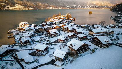 View of Iseltwald village covered in snow, mountains and Bierzensee during sunset on a winter day in Switzerland.