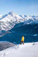 Caucasian man standing on top of a hill looking at winter snow mountain landscape and forests on a sunny day around St. Moritz, Switzerland.
