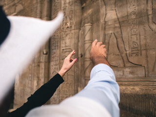 Hands of white caucasian man and woman pointing at Egyptian hieroglyphs on a wall.
