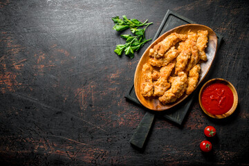 Chicken strips on a cutting Board with parsley and tomato sauce in a bowl.