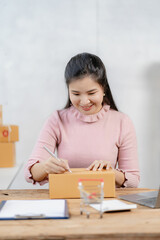 Asian businesswoman starting a successful small business Freelance work from home with laptop online shopping with online parcel delivery service, SME concept and package delivery.