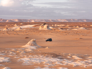 Dark jeep 4x4 driving through the landscape of White Desert, Egypt during sunset. 