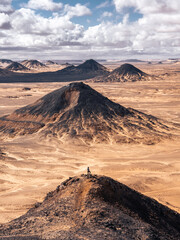 Woman standing on top of a volcanic hill looking at landscape in Black Desert, Egypt.