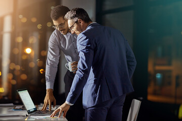 Teamwork, review and night with business people at laptop for project management, planning or web design. Collaboration, goal and documents with employee in digital agency for marketing strategy