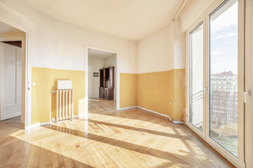 Empty room with varnished vintage wooden floors, large windows with views and access to balconies and smooth walls, oak flooring and cast iron radiators