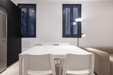 Dining room with white wooden table with matching chairs and blue wooden windows overlooking an interior brick patio