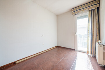 Empty living room with two triple-paned aluminum windows, red stoneware floors and electric heat accumulator and exit to a terrace with curtains on the door
