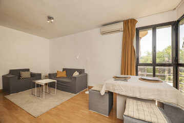 A furnished living room with a table set, rugs under the sofas and a window with orange curtains