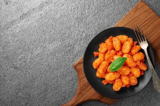 A plate of POTATO GNOCCHI in tomato sauce and a basil leaf on a cutting board. Gray stone background. View from above. Copy space.