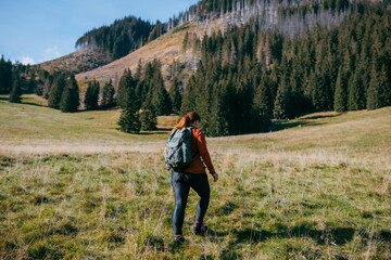 Fototapeta na wymiar Back view of stylish woman wearing green backpack and red hat looking at mountain view while relaxing in nature. Travel and wanderlust concept. Amazing chill moment