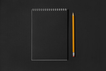 Blank notebook with blank black sheets and yellow pencil on dark background, copy space, top view. Business or education concept.