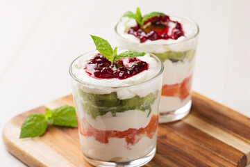 Dessert of cottage cheese cream, orange, kiwi, decorated with mint in glasses on a light wooden table.  Healthy breakfast.