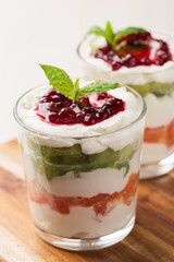 Dessert of cottage cheese cream, orange, kiwi, decorated with mint in glasses on a light wooden table.  Healthy breakfast. Vegetarian organic dessert. Vertical orientation.