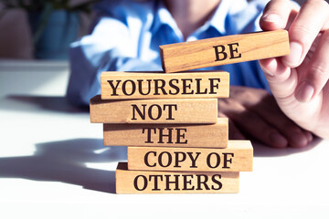 Close up on businessman holding a wooden block with "Be Yourself Not The Copy of Others" message