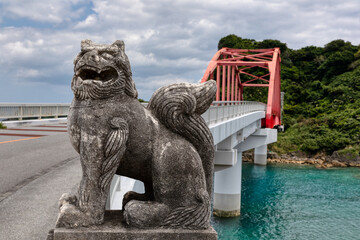 Large stone shisa lion guards the red bridge to Ikei Island, Okinawa, Japan.
