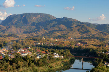 Fototapeta na wymiar Scenery view small town of Luang Prabang city center surround big mountain and Mekong river, Cityscape in the evening with golden sunlight during sunset, The ancient capital province in northern Laos.