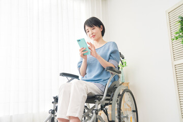 Fototapeta na wymiar 家でスマホを使う車椅子に乗った障がい者女性