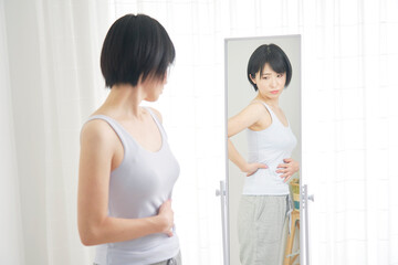 Fototapeta na wymiar 鏡を見て体型に悩む女性