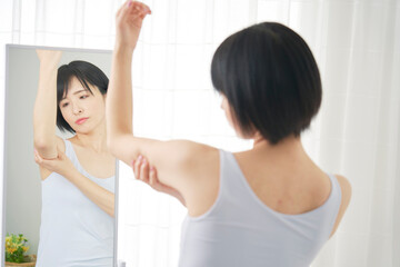 Fototapeta na wymiar 鏡の前で二の腕の贅肉を摘む女性