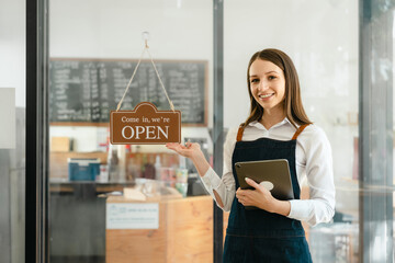 Young friendly female pretty caucasian coffee shop woman owner in apron with open sign, small business owners smiling and service take away orders from food delivery application on tablet.