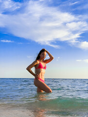 A young beautiful woman with long hair in a swimsuit dreamily looks at the beach with the sea in the background