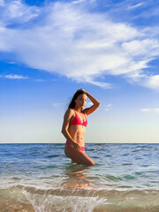 A young beautiful woman with long hair in a swimsuit dreamily looks at the beach with the sea in the background - 562415842