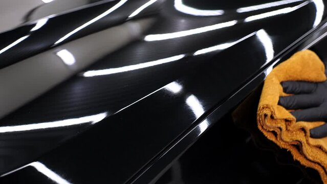 Close-up of a man polishing a shiny black car with microfiber in a modern car showroom. The concept of detailing the car.
