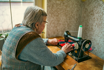 Senior woman in spectacles use sewing machine. wrinkled hands of the old seamstress.elderly woman ....