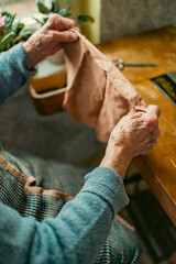 Senior woman in spectacles use sewing machine. wrinkled hands of the old seamstress.elderly woman . Old sewing machine Classic retro style manual sewing machine ready for sewing work.