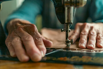 Senior woman in spectacles use sewing machine. wrinkled hands of the old seamstress.elderly woman . Old sewing machine Classic retro style manual sewing machine ready for sewing work.