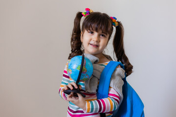 a happy little preschool girl with a backpack and a globe on a light background, space for text. Preschool education, traveling with children