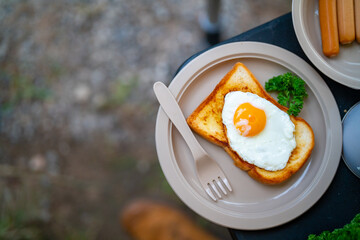 Breakfast on the table. Asian couple cooking food fried egg and bread with sausage at camp. Man and woman enjoy outdoor lifestyle travel nature and camping together on summer holiday vacation.
