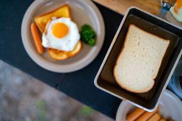 Breakfast on the table. Asian couple cooking food fried egg and bread with sausage at camp. Man and woman enjoy outdoor lifestyle travel nature and camping together on summer holiday vacation.