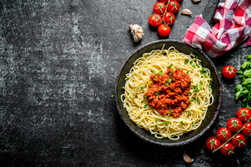 Spaghetti with Bolognese sauce in pan with a napkin and tomatoes.