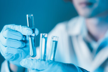 Scientist hand hold test tubes filled with blue sample chemicals in chemistry science laboratory. Glassware in medical research. Scientific lab for Biotechnology.