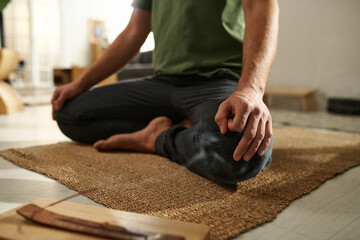 Close-up of young man sitting on carpet in lotus position and meditating