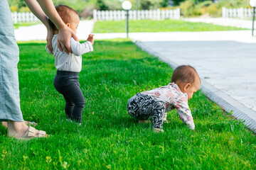 Mother teaching babies to take first steps on lawn