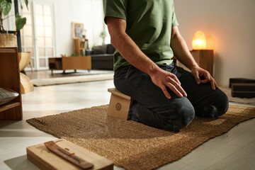 Close-up of young man sitting on carpet in the room and meditating with aroma stick