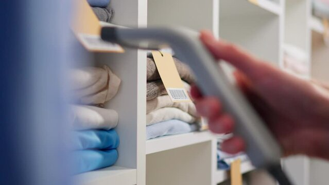 The process of scanning barcodes on a clothing tag, Close-up of an electronic scanner red beam, An employee of fashion store being at her workplace, takes stock of goods on the shelves of a store rack