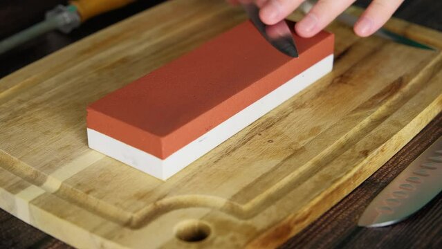 Man sharpening a knife at home using a sharpening whetstone, slow motion video of process, sanding stone block for chefs and home cooks, 4k high quality video footage
