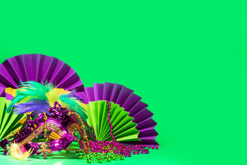 Mardi Gras colourful holiday greeting card background with festival masquerade accessories, decor, carnival mask, beads, feathers, fan on bright background traditional yellow purple green colors