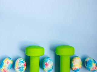 green heavy dumbbells, colorful easter eggs on blue background. Easter fitness