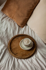 Hot mug of cappuccino on wooden tray on the bed, breakfast. Cozy house. Beige natural colors. Aesthetic.