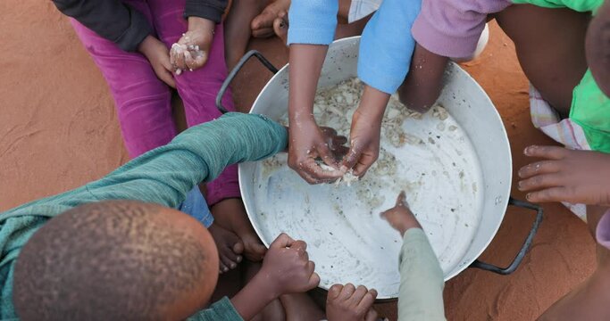 Poverty in Africa. Small group of starving Black African children scraping food from the bottom of a communal cooking pot