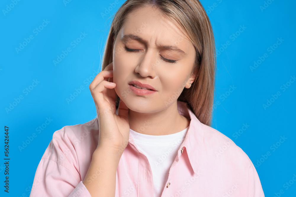 Wall mural Young woman suffering from ear pain on light blue background