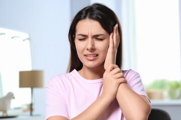 Young woman suffering from ear pain indoors - obrazy, fototapety, plakaty