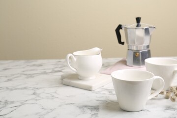 Cups, moka pot and jug on white marble table. Space for text