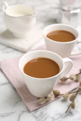 Cups of hot aromatic coffee and willow branches on white marble table